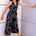 A woman modeling a sleeveless black jumpsuit with a v-neck and retro geometric print, standing against a wall.