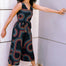 A woman modeling a sleeveless black jumpsuit with a v-neck and retro geometric print, standing against a wall.