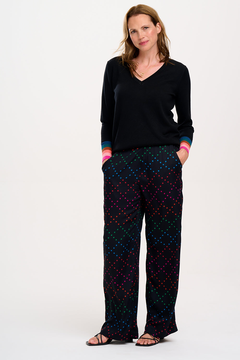 A person standing wearing black trousers with a colorful geometric star pattern on the lower half, paired with a black top and sandals.