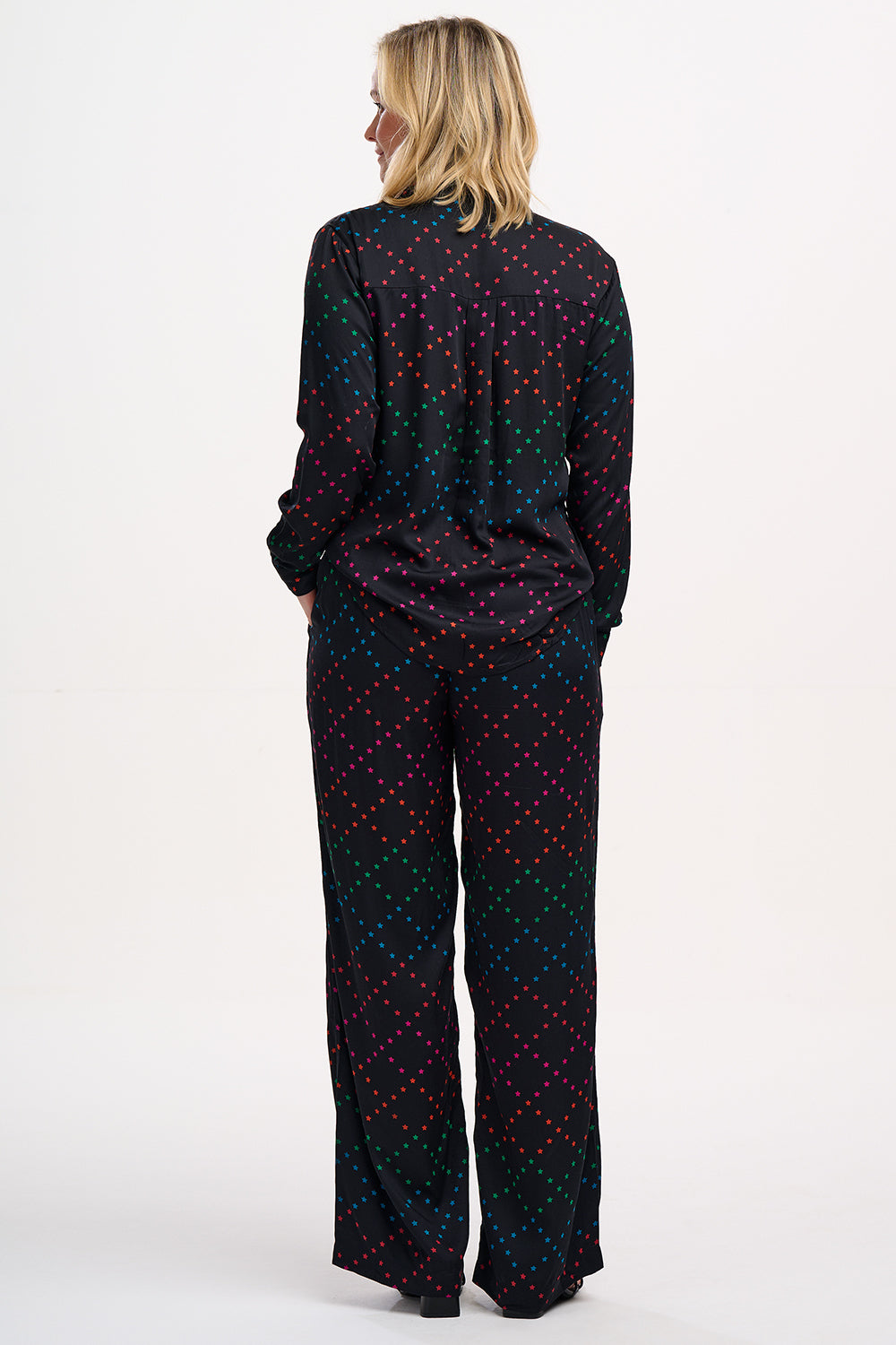 A person standing wearing black trousers with a colorful geometric star pattern on the lower half, paired with a black top and sandals.