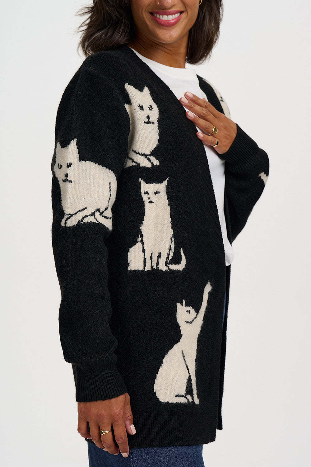 A woman wearing a black knit cardigan sweater with cream-colored cat motifs knitted all over it, layered over a white top.
