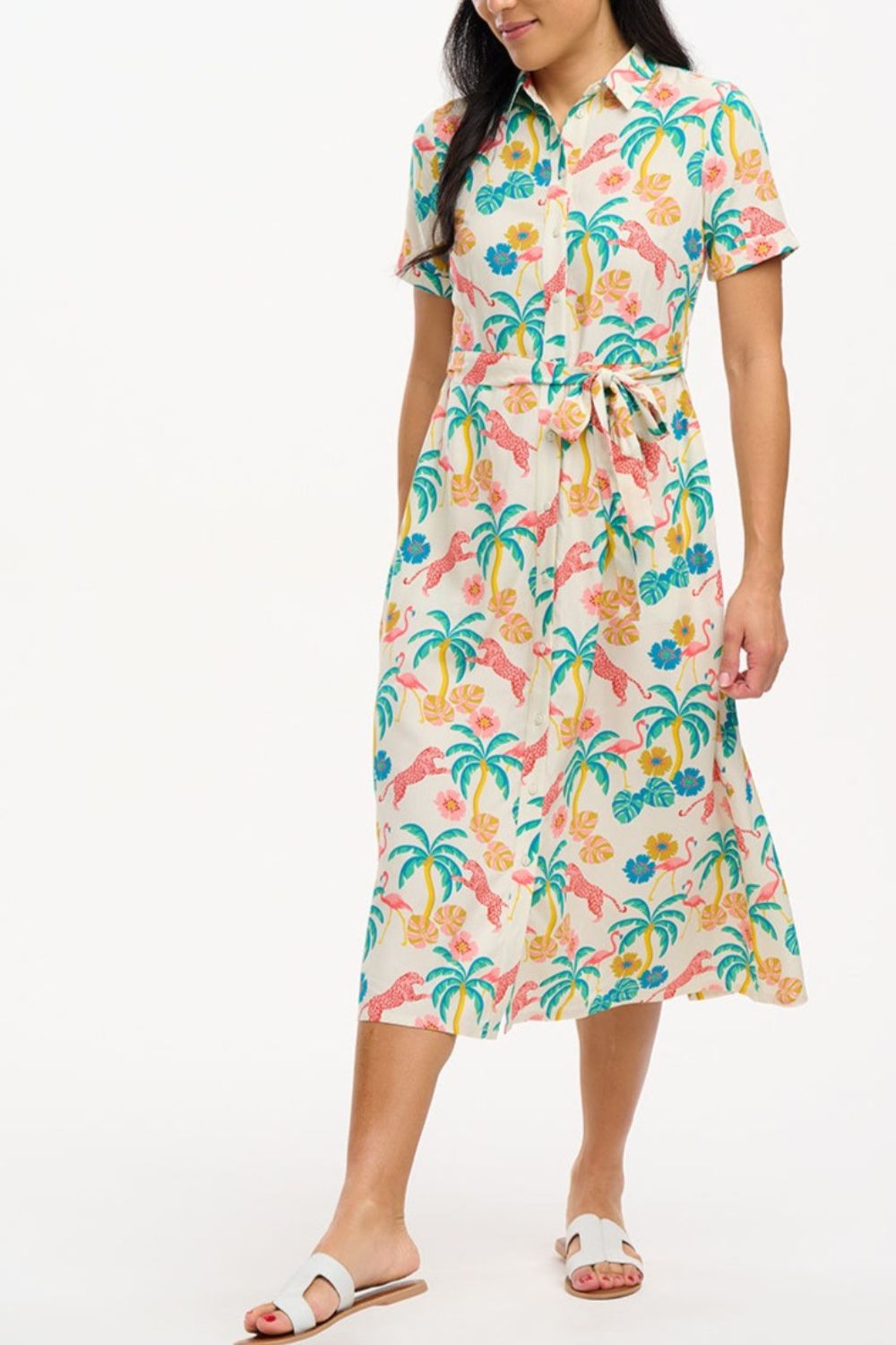 A woman wearing an off-white shirt dress with a colorful floral print, featuring a button-up front, a shirt collar, and a tie waist belt.