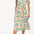 A woman wearing an off-white shirt dress with a colorful floral print, featuring a button-up front, a shirt collar, and a tie waist belt.