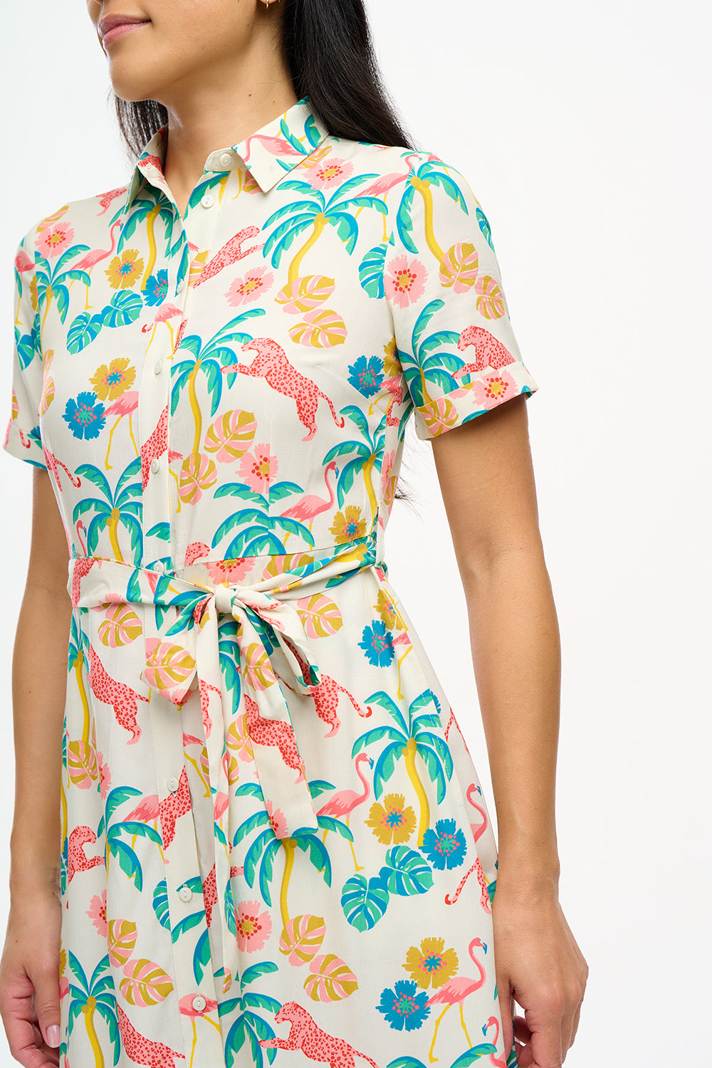 A woman wearing an off-white shirt dress with a colorful floral print, featuring a button-up front, a shirt collar, and a tie waist belt.