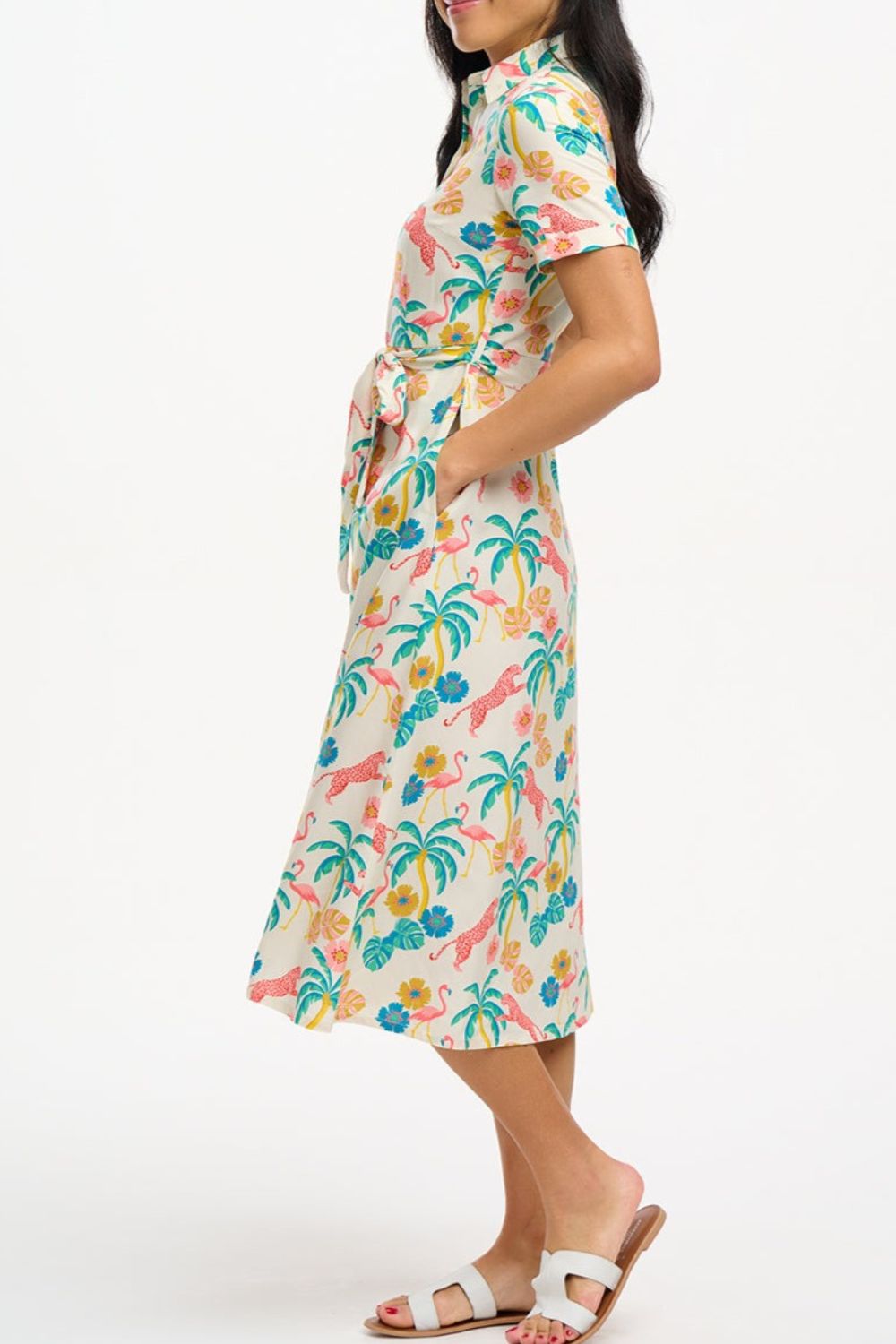 A woman wearing an off-white shirt dress with a colorful floral print, featuring a button-up front, a shirt collar, and a tie waist belt.