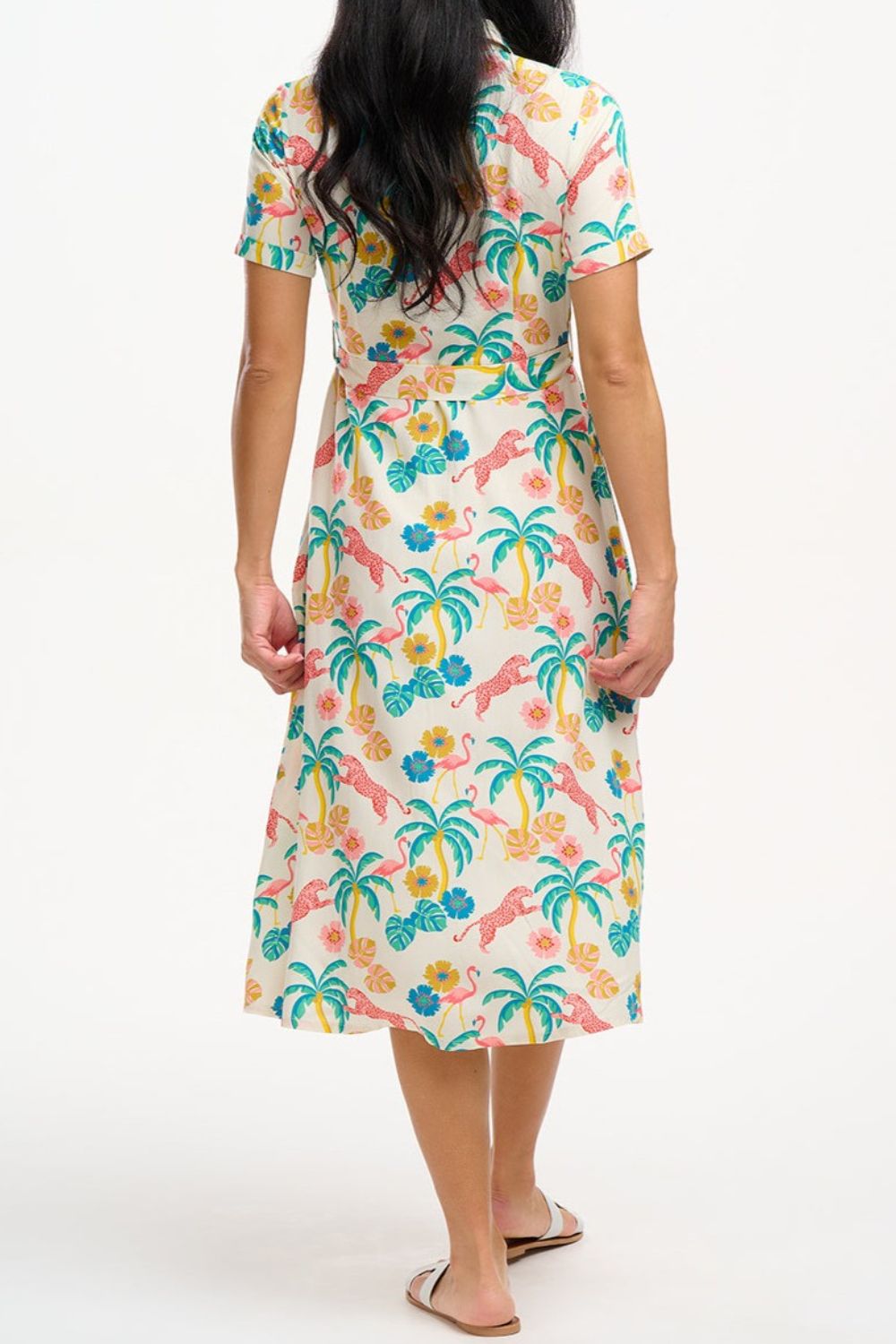 A woman wearing an off-white shirt dress with a colorful floral print, featuring a button-up front, a shirt collar, and a tie waist belt.