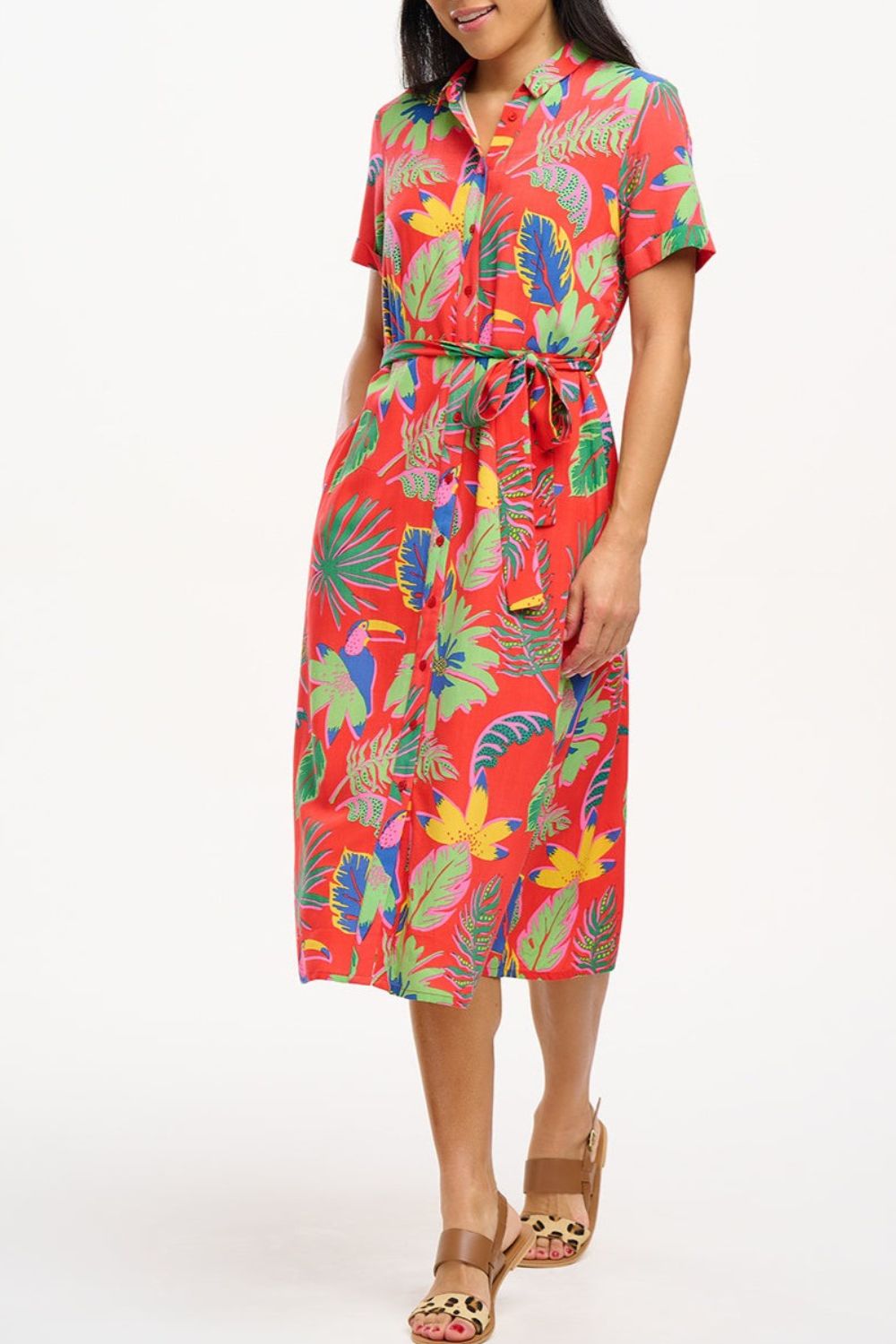 A woman wearing a red shirt dress with a Tropical Toucans print, featuring a button-up front, a shirt collar, and a tie waist belt.