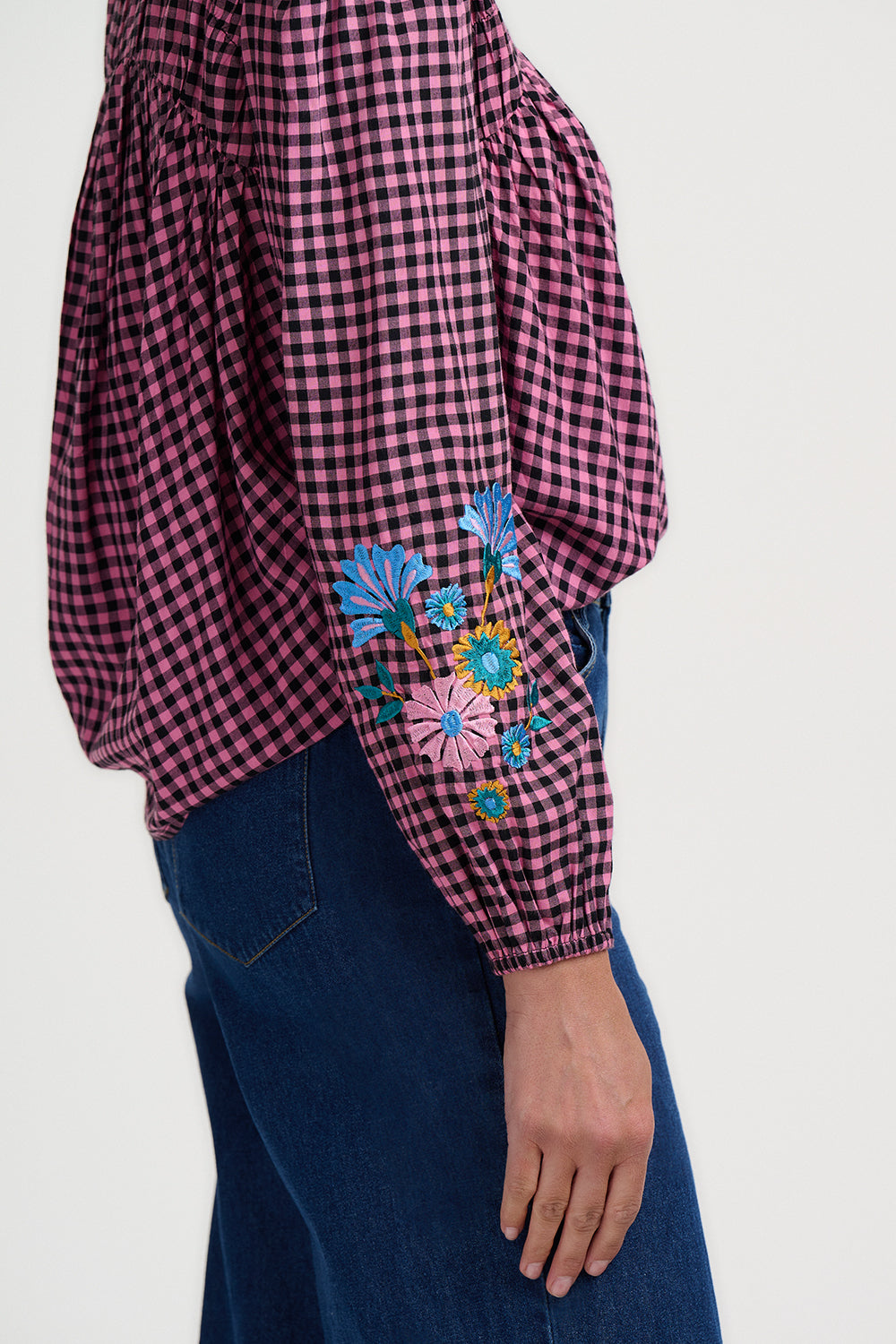Checkered shirt with floral embroidery on sleeves and blue jeans against a white background