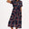 A model wearing a midi length shirt dress with a traditional shirt collar, button placket, and a full skirt with an elasticated waist. The dress has a black base with a 70s-inspired geometric retro print in red and pink.