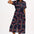 A model wearing a midi length shirt dress with a traditional shirt collar, button placket, and a full skirt with an elasticated waist. The dress has a black base with a 70s-inspired geometric retro print in red and pink.