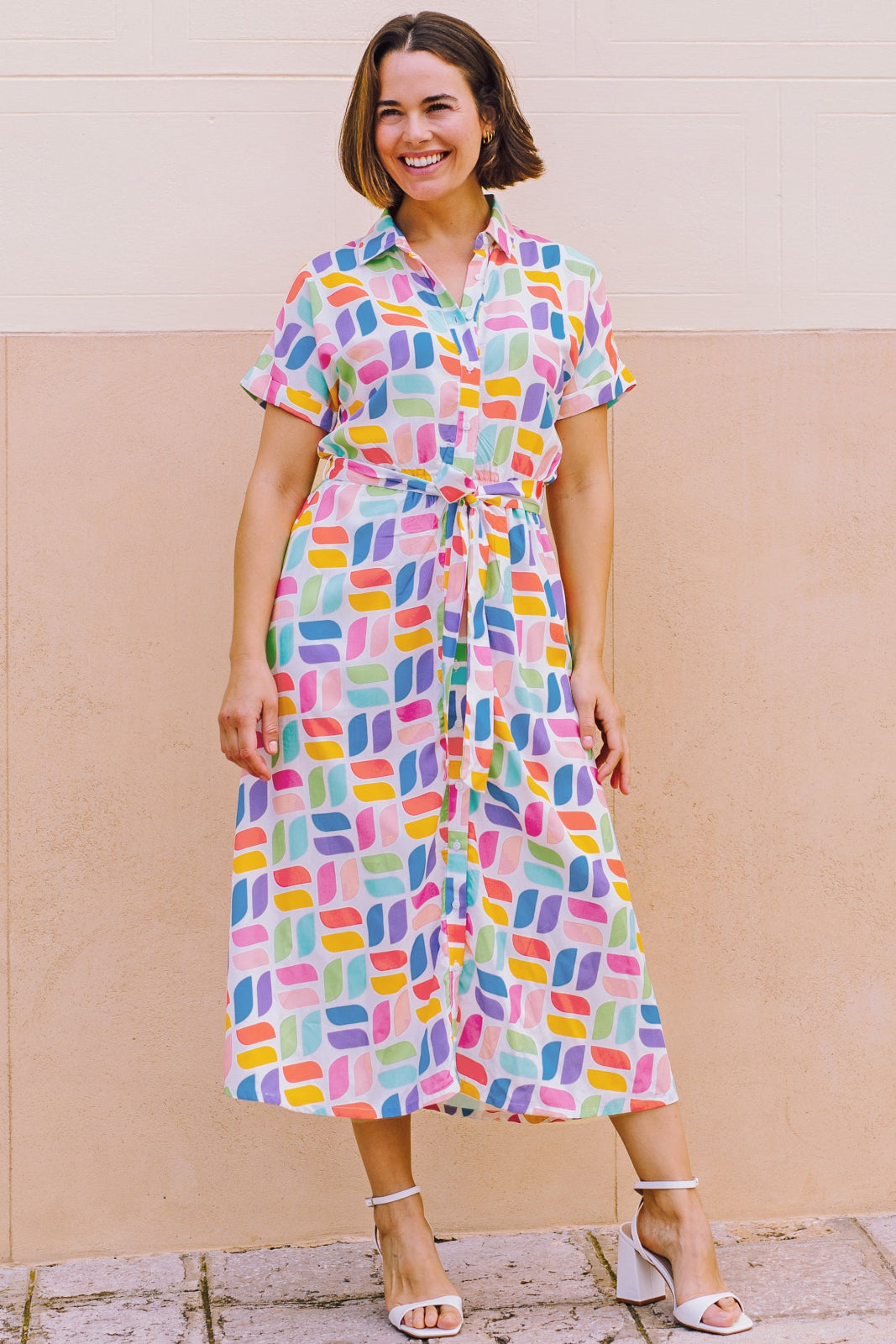 A model wearing an off-white midi shirt dress with a curved geometric print, featuring a traditional shirt collar, button placket, and elasticated waist.