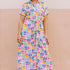 A model wearing an off-white midi shirt dress with a curved geometric print, featuring a traditional shirt collar, button placket, and elasticated waist.