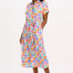 A model wearing an off-white midi shirt dress with a curved geometric print, featuring a traditional shirt collar, button placket, and elasticated waist.