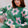 Woman wearing a green sweater with pink floral patterns, sitting on a chair.