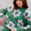 Woman wearing a green sweater with pink floral patterns, sitting on a chair.