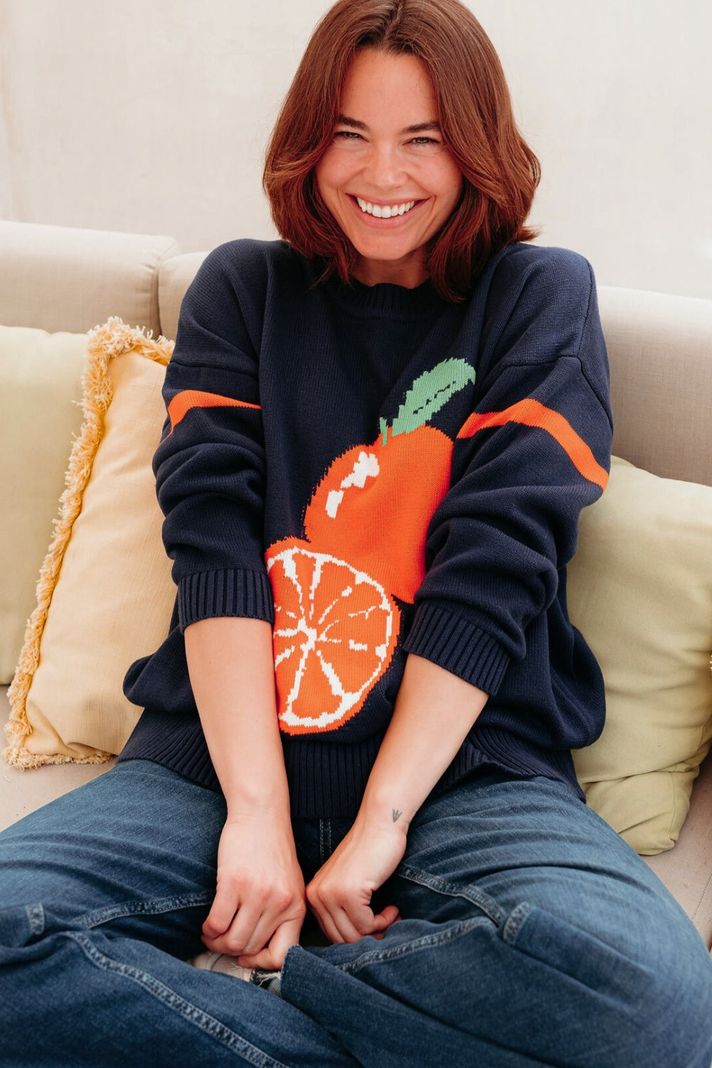 Person wearing a navy sweater with an orange design, sitting on a beige couch.