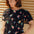 A model wearing a black jersey t-shirt with a floral and hummingbird print, round neckline, and short puffed sleeves.