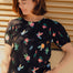 A model wearing a black jersey t-shirt with a floral and hummingbird print, round neckline, and short puffed sleeves.
