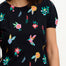 A model wearing a black jersey t-shirt with a colorful hummingbird and garden design, with short puffed sleeves and a round neckline.