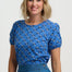 Woman wearing a blue floral top and denim skirt on a white background