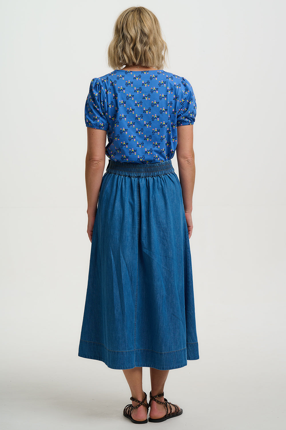Woman wearing a blue patterned top and blue denim skirt on a white background