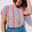 A woman smiling and posing in a multicolored jersey top with a geometric pattern of rainbow circles, paired with a denim skirt.