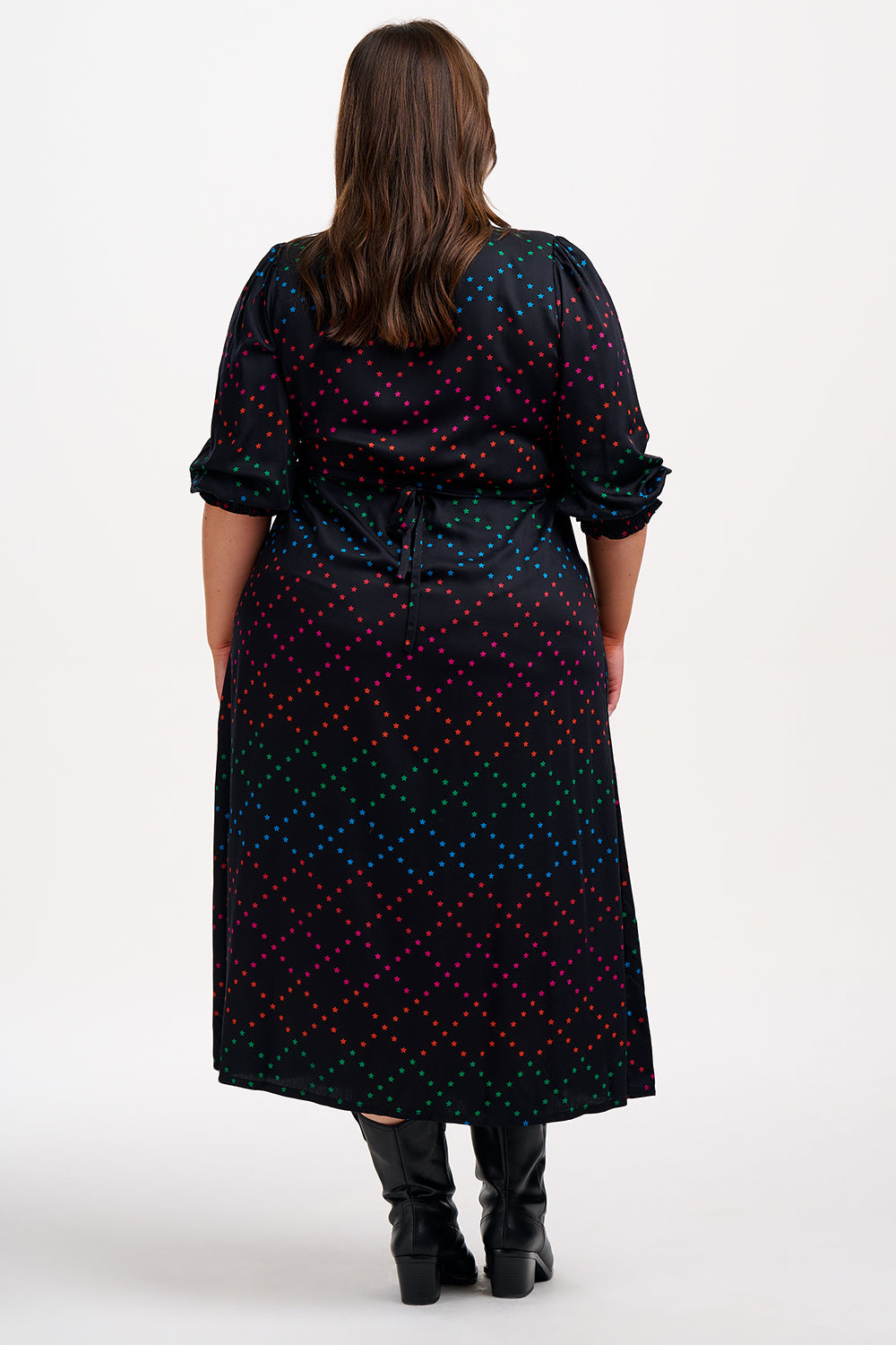A woman standing and posing in a black and rainbow star lattice print midi dress with three-quarter length sleeves and a scoop neck.