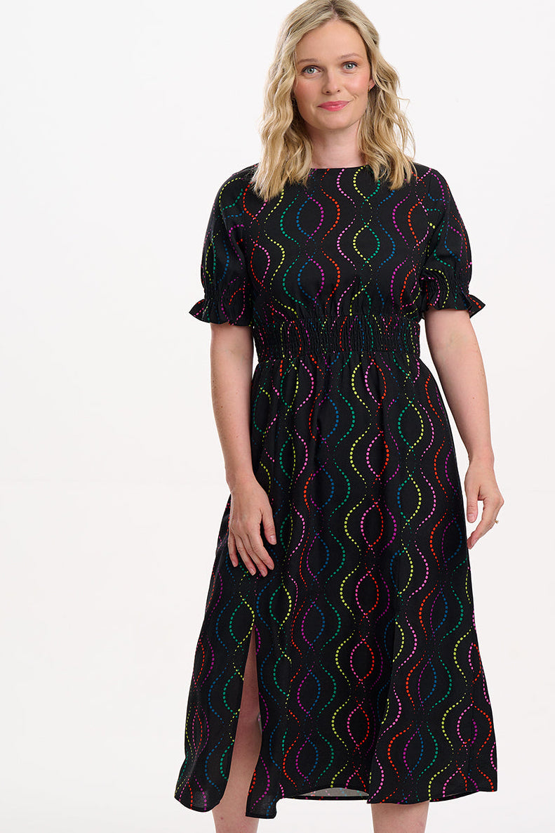 Sugarhill Brighton model wearing a black dress with colourful pattern on a white background