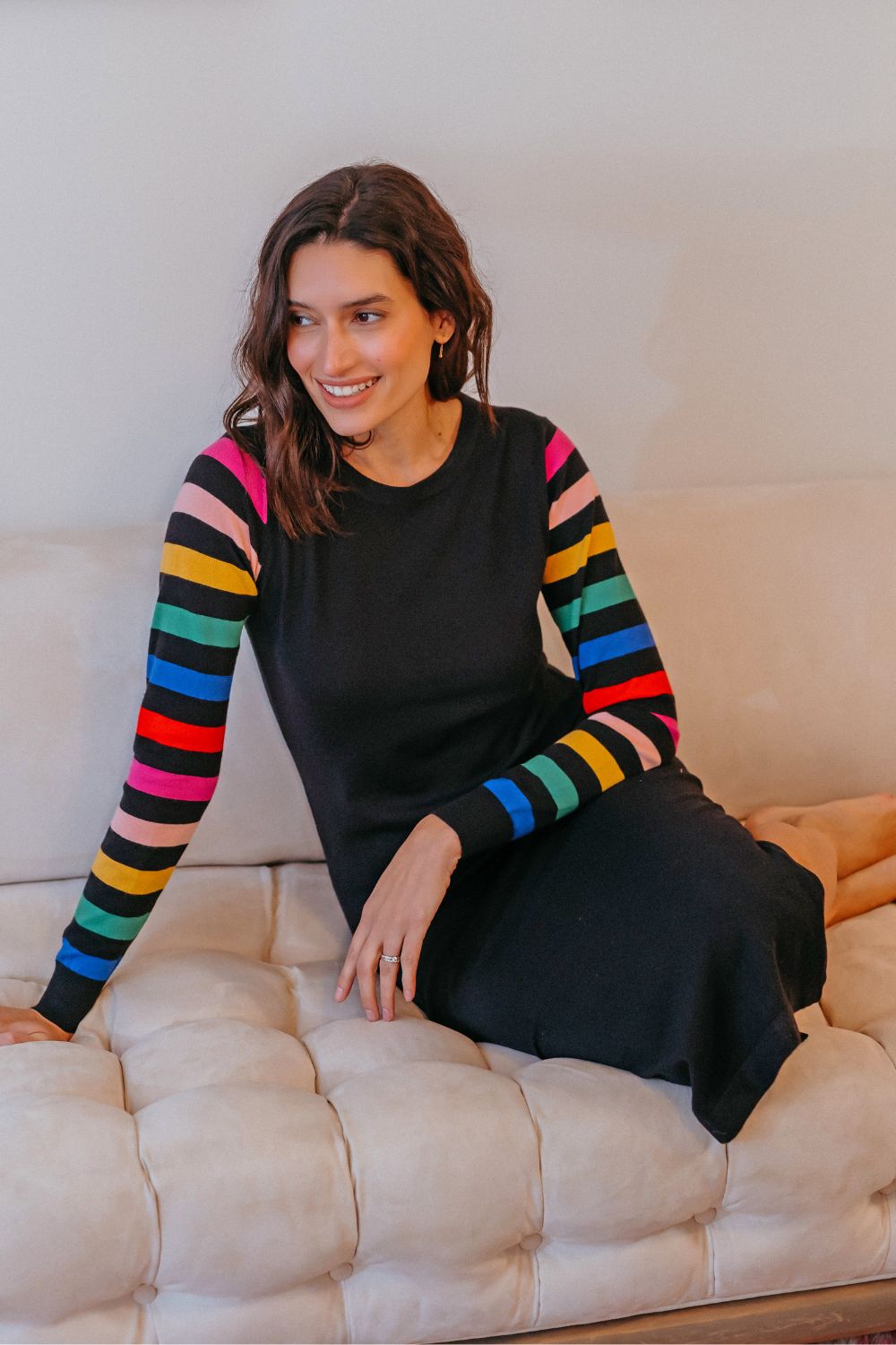 Woman wearing a black dress with colorful sleeves sitting on a beige couch.