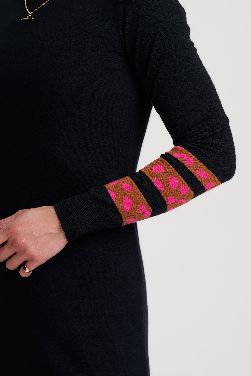 Person wearing a black long-sleeve top with pink and brown patterned arm sleeves on a white background