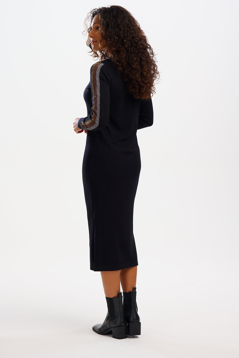 A model wearing a black midi knit dress with metallic stripes on the sleeves, paired with black boots.