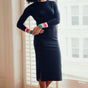 Woman wearing a black dress with colorful arm sleeves standing in a room with a window.