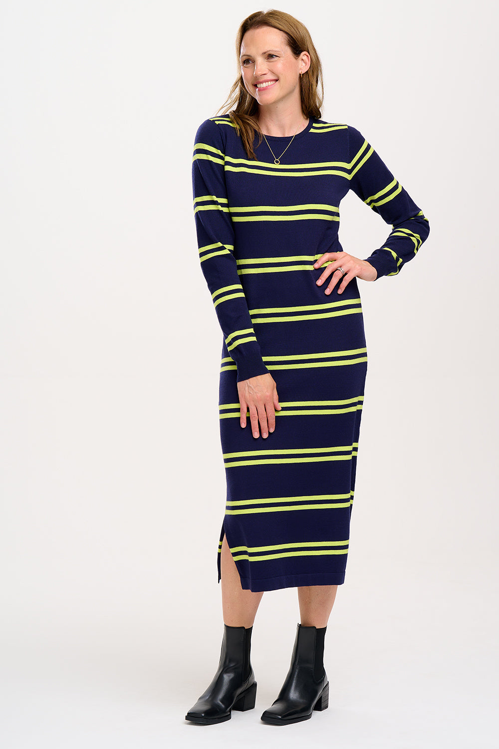 A model wearing a navy knit dress with green double stripes, long sleeves, and a crew neck. The dress has a semi-fitted silhouette and a split side hem.