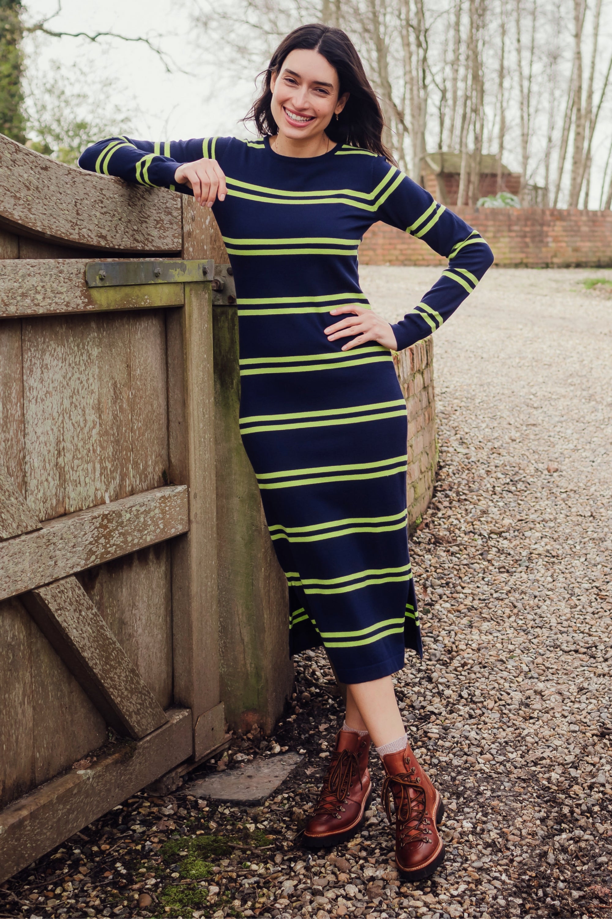 A navy, double-striped midi knit dress with long sleeves and a crew neck, displayed against an outdoor backdrop.