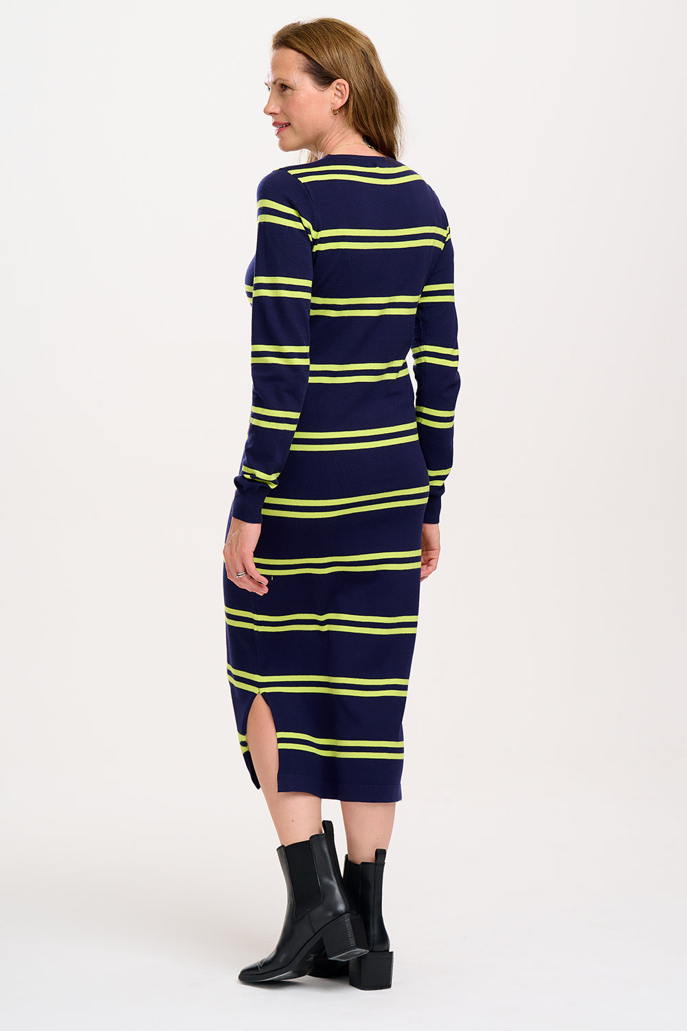 A model wearing a navy knit dress with green double stripes, long sleeves, and a crew neck. The dress has a semi-fitted silhouette and a split side hem.