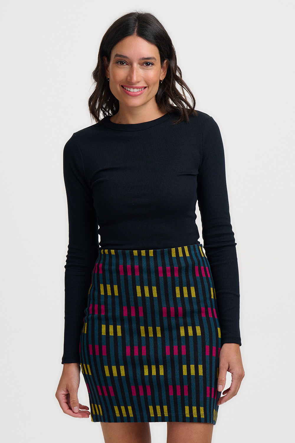 Woman wearing a black long-sleeve top and colorful patterned skirt on a white background