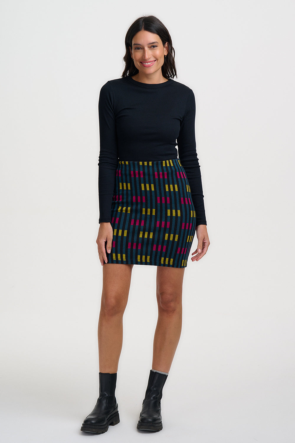 Woman wearing a black long-sleeve top and patterned skirt on a white background