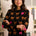 Woman wearing a black sweater with colorful cat pattern in a room with children's drawings on the wall.