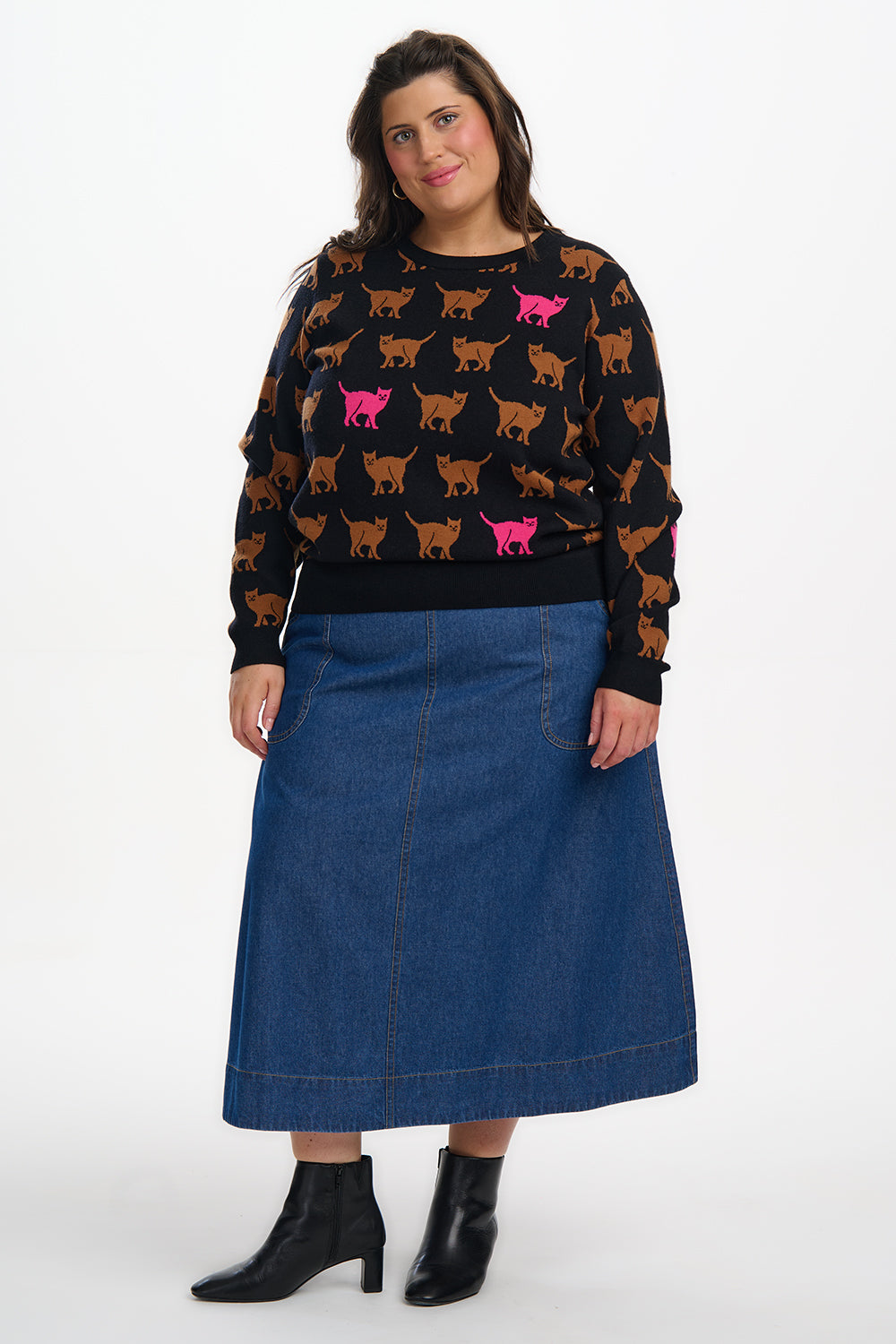 Woman wearing a black sweater with colorful cat patterns and a blue denim skirt on a white background