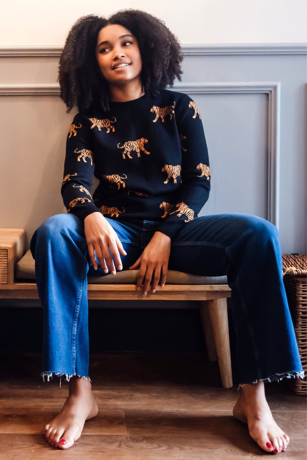 Woman sitting on a bench wearing a black sweater with animal prints and blue jeans.