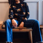 Woman sitting on a bench wearing a black sweater with animal prints and blue jeans.