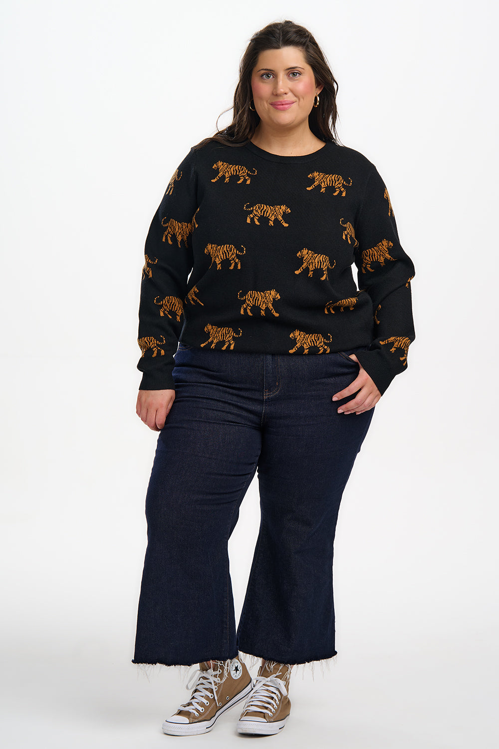 Person wearing a black sweater with tiger patterns and dark blue jeans on a white background