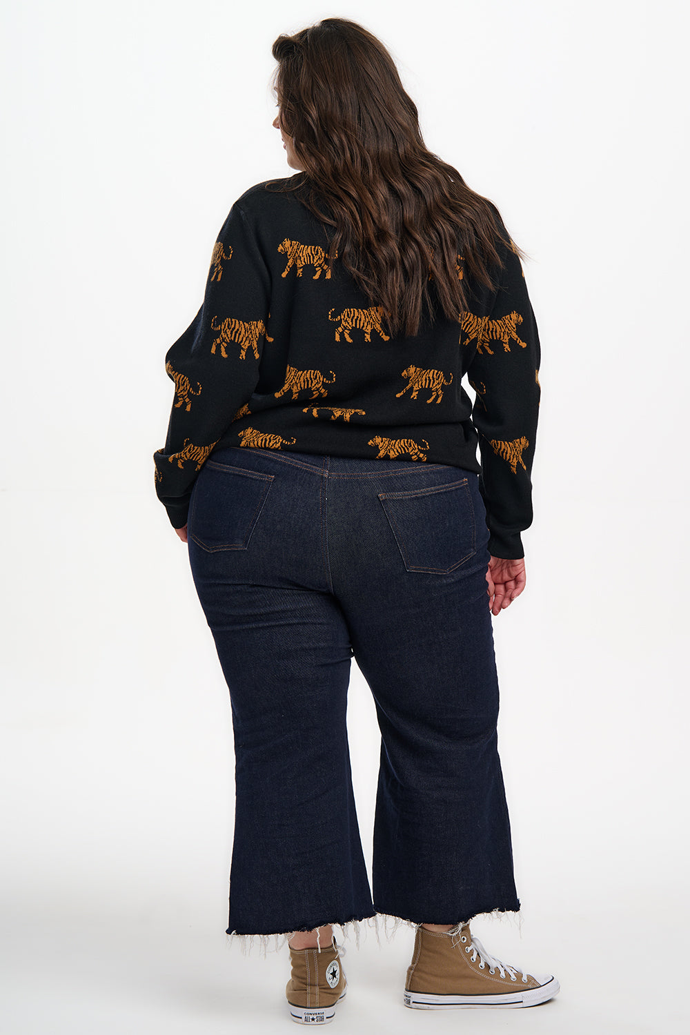 Person wearing a black sweater with orange tiger patterns and dark jeans on a white background