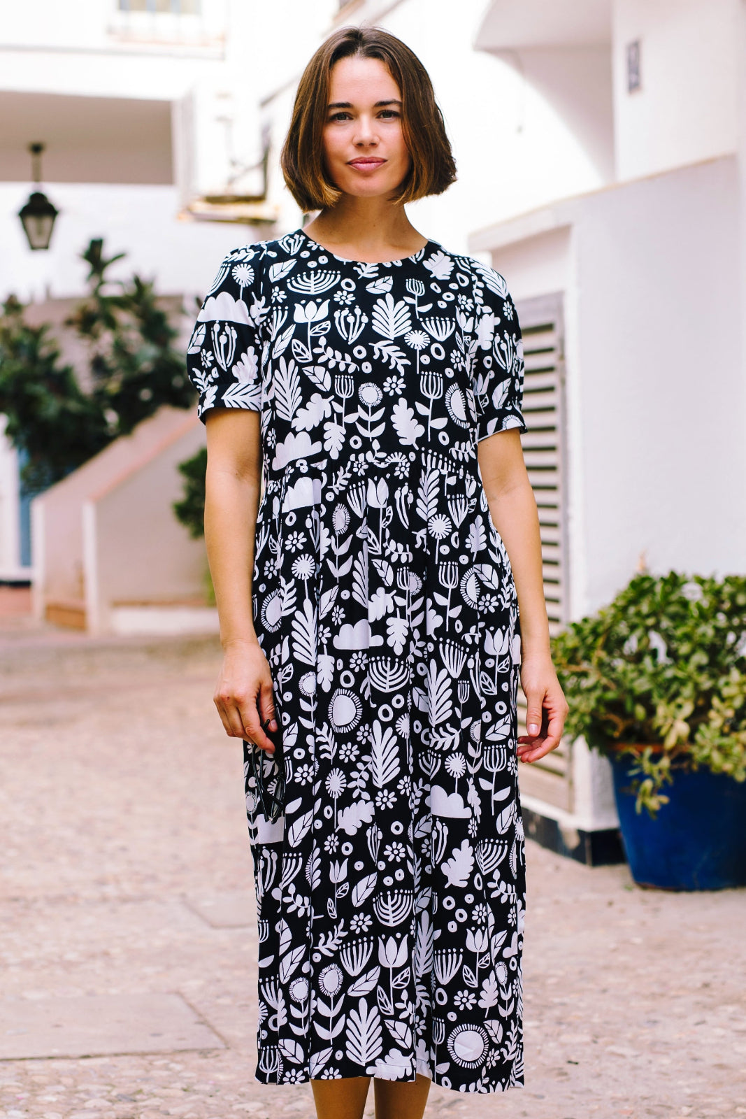 A model wearing a monochrome black and white floral folk print midi dress with short sleeves and a round neckline.