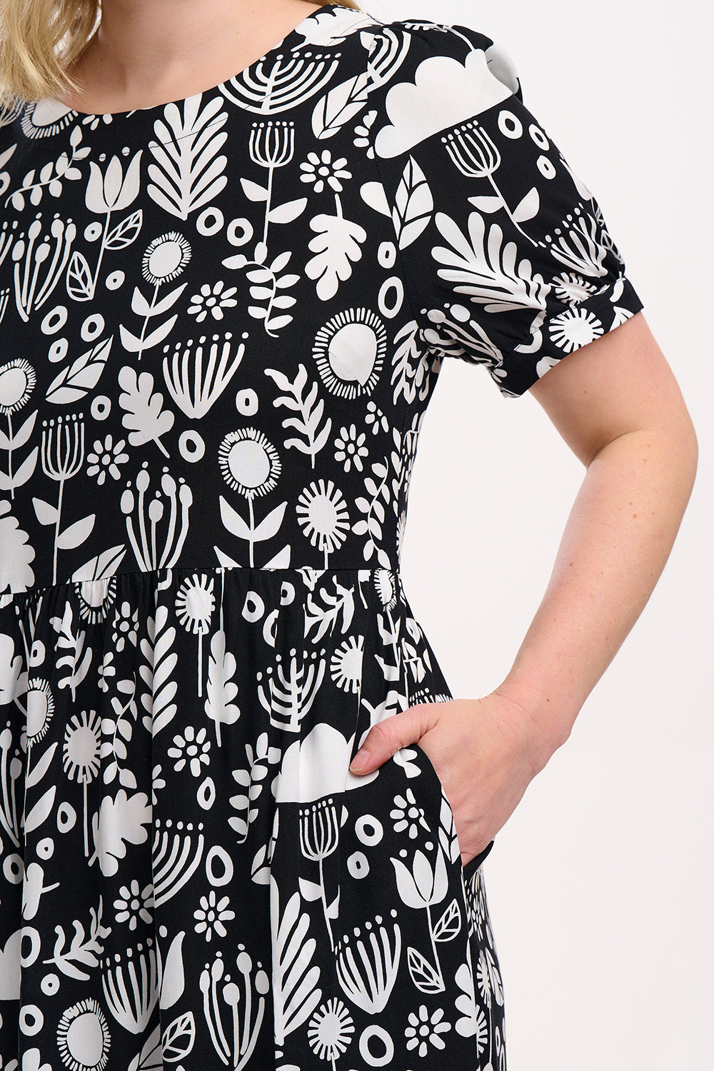 A model wearing a monochrome floral folk print midi dress with short blouson sleeves and a round neckline.