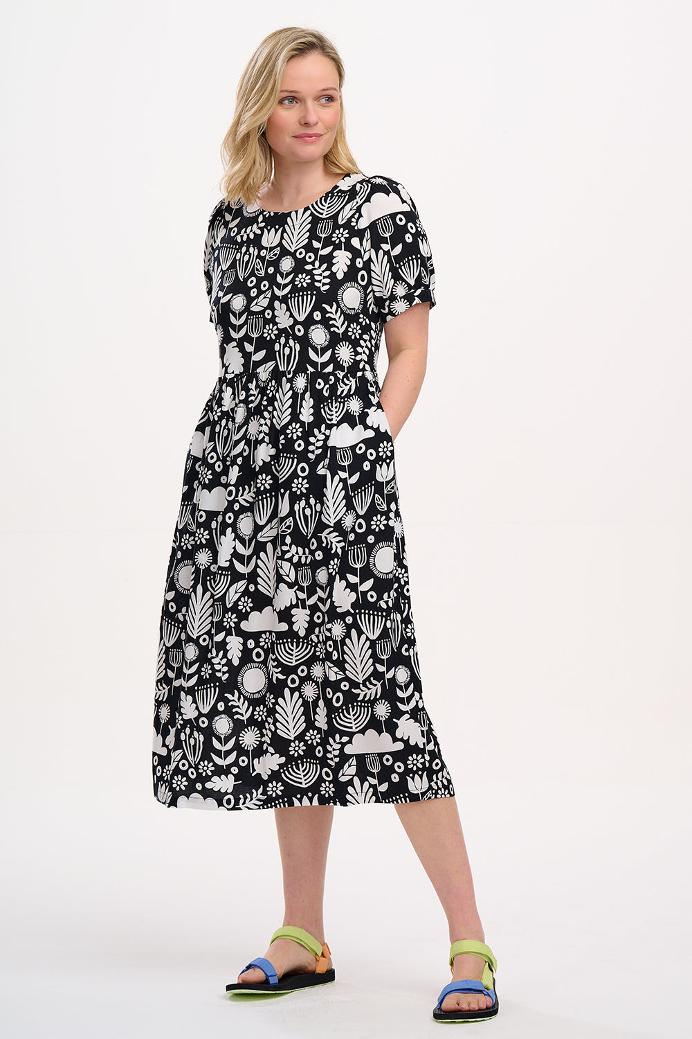 A model wearing a monochrome floral folk print midi dress with short blouson sleeves and a round neckline.