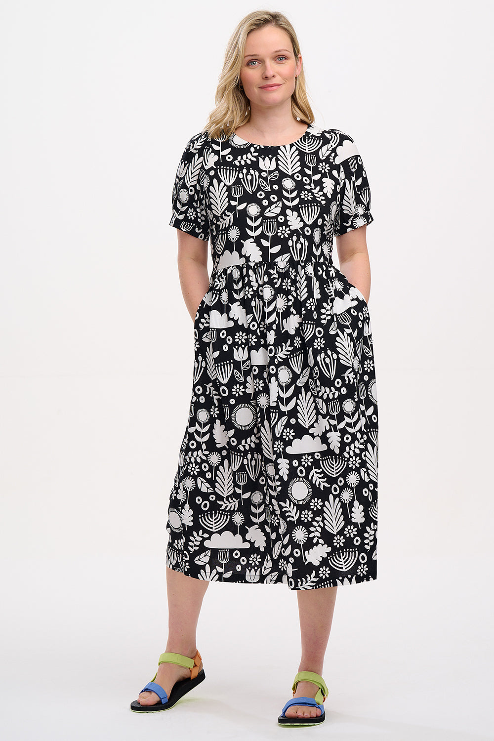 A model wearing a monochrome floral folk print midi dress with short blouson sleeves and a round neckline.