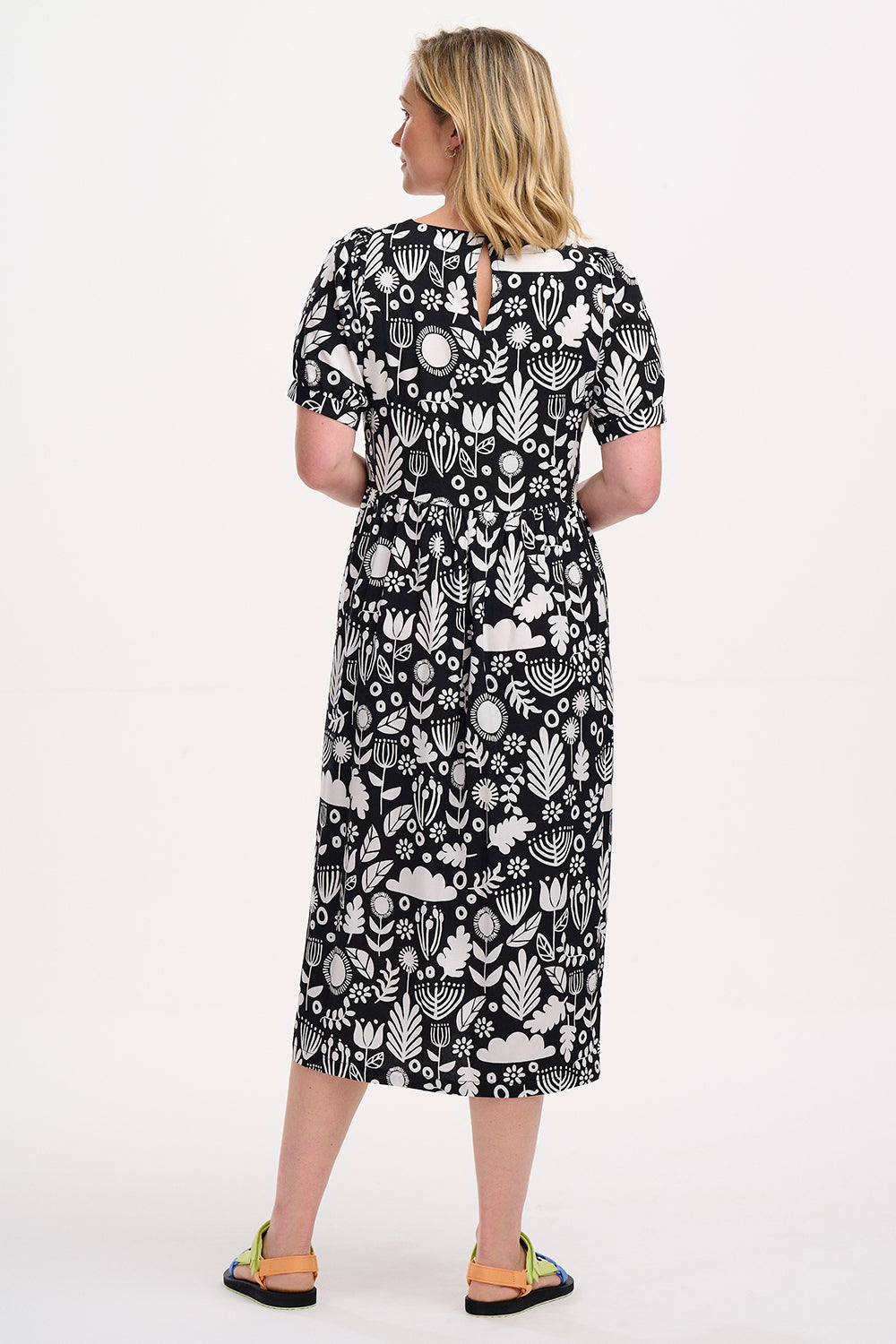A model wearing a monochrome floral folk print midi dress with short blouson sleeves and a round neckline.