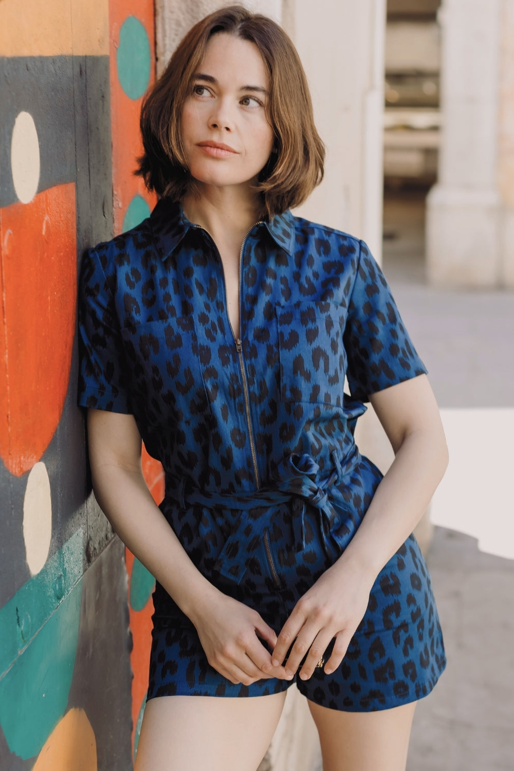 Woman wearing a blue leopard print outfit against a colorful wall.