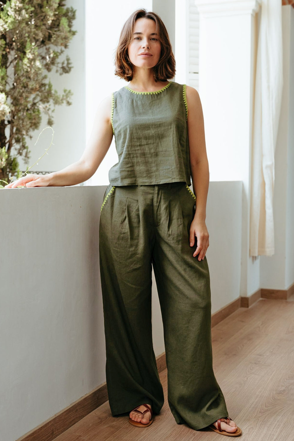 Woman wearing a green sleeveless top and wide-leg pants standing indoors.